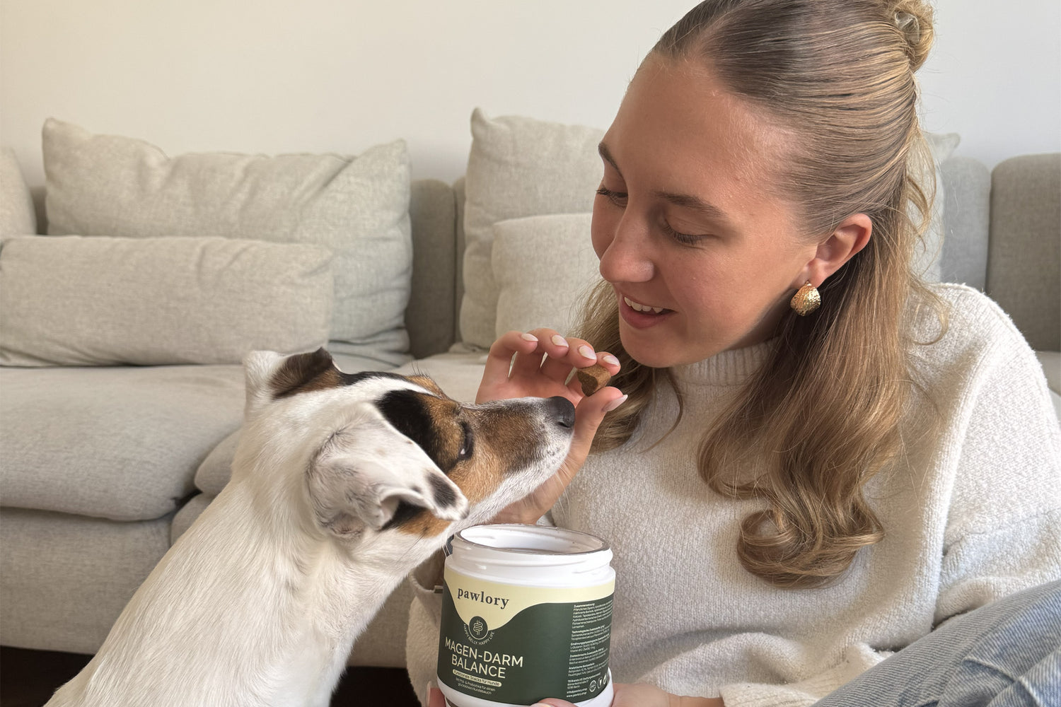 Hundebesitzerin sitzt auf dem Sofa und füttert ihrem Hund einen Pawlory Magen-Darm Balance Snack direkt aus der geöffneten Dose – ein natürlicher Moment, der Vertrauen und hohe Akzeptanz des Produkts zeigt.
